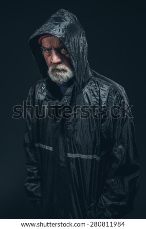 Half Body Shot of a Serious Bearded Senior Man Wearing Black Raincoat, Staring at the Camera. Isolated on Black Background.