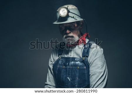 Close up Middle Age Male Mine Worker with Turned on Light on his Helmet, Looking at the Camera Seriously Against Gray Gradient Background.