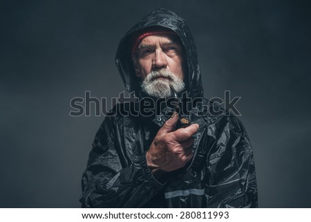Portrait of a Contemplative Bearded Old Guy Holding a Tobacco Pipe While Looking Into Distance Against Fuzzy Black Background.