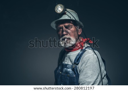 Close up Senior Male Mining Worker with Dirt on Face, Smoking a Cigarette While Looking Straight at the Camera Against Gray Background