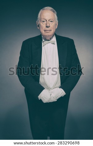 Senior Male Butler Wearing Formal Tuxedo Suit and White Gloves Standing at Attention Ready for Service and Looking at Camera