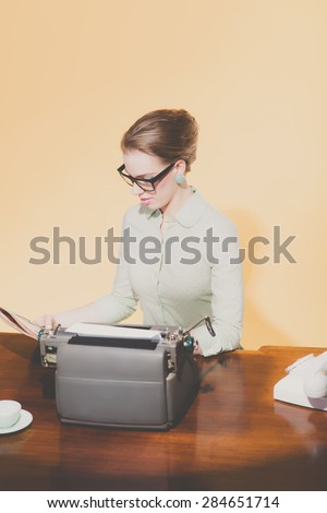 Vintage 1950 young secretary sitting behind desk reading newspaper.