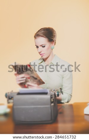 Retro 1950 young secretary woman sitting behind desk reading magazine.