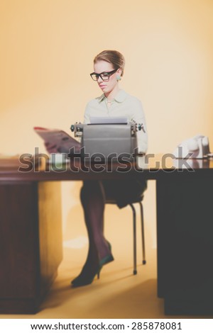 Magazine reading retro 1950 young secretary sitting behind desk with typewriter.