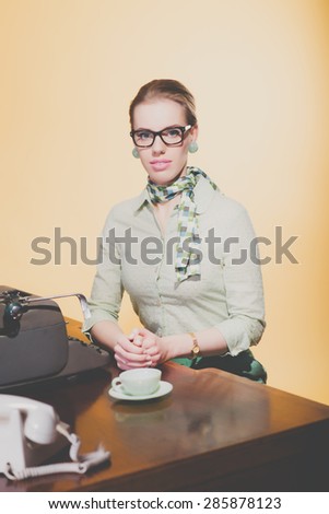 Vintage 1950 young secretary woman behind desk with typewriter wearing black glasses. High angle view.