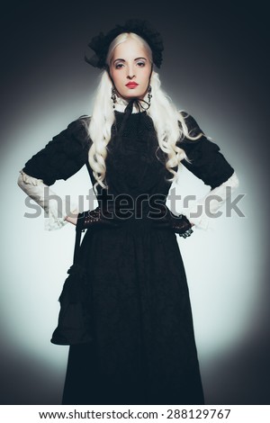 Dramatic Portrait of Woman with White Hair Dressed in Black - Woman Wearing Victorian Style Gown, Gloves and Hat Standing with Hands on Hips