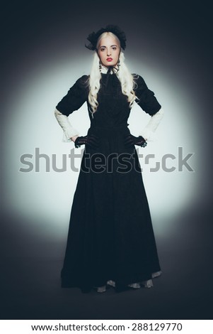Dramatic Full Length Portrait of Woman with White Hair Dressed in Black - Woman Wearing Floor Length Victorian Style Gown, Gloves and Hat Standing with Hands on Hips