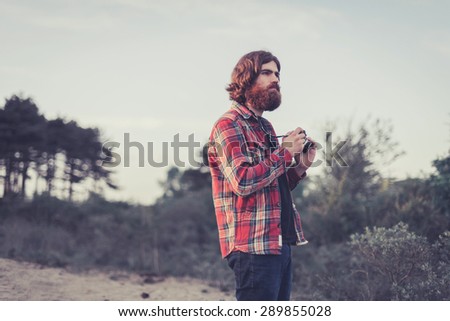 Handsome male backpacker with a camera in the wilderness following his hobby and passion for photography, upper body staring thoughtfully into the distance