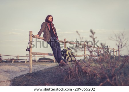 Backpacker relaxing admiring the view standing leaning on a wooden rail fence on a hilltop in the distance, with copyspace