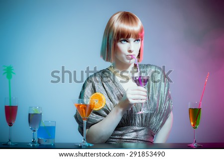 Glamorous Woman with Red Hair Wearing Shiny Retro Gown and Sipping Cocktail Drink from Straw, Standing at Bar in Disco Night Club