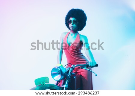 Elegant Young Woman Posing on her Vintage Motorcycle While Smoking a Cigarette Against White Background.