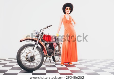 Stylish Young Woman in Orange Dress, Posing on her Vintage Motorcycle on a Checkered Floor Against White Background.