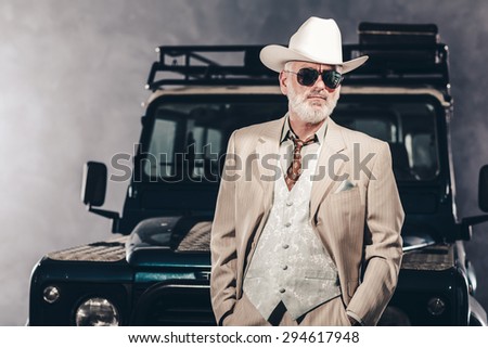 Good Looking Senior Man Wearing Formal Fashion with White Cowboy Hat and Sunglasses, Posing Against his Vintage 4x4 Vehicle.