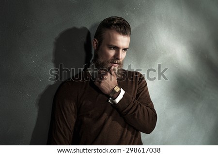 Thoughtful worried bearded young man with his hand to his chin standing staring at the floor, upper body portrait