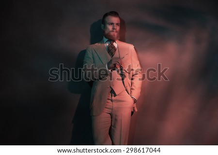 Handsome sexy bearded man in a stylish suit standing leaning against a wall in red toned atmospheric lighting, with copyspace