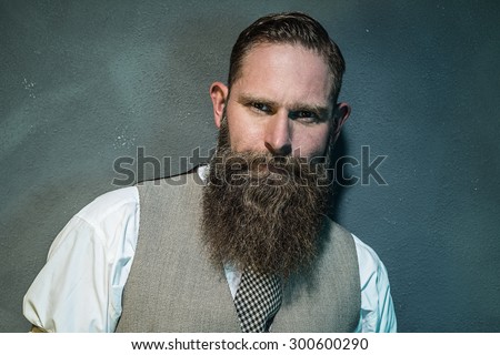 Close up Gorgeous Adult Man with Long Goatee Beard Looking Fierce at the Camera Against Gray Wall.