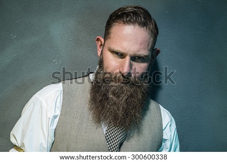 Close up Gorgeous Adult Man with Long Goatee Beard Looking Fierce at the Camera Against Gray Wall.