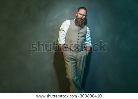 Three Quarter Shot of a Pensive Bearded Man in Formal Wear Looking Into the Distance with Hands in the Pockets Against Gray Wall.