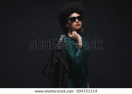 Half Body Shot of a Stylish Young Woman with Afro Hair, Holding her Jacket over the Shoulder against Dark Background.