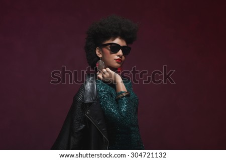 Half Body Shot of a Stylish Young Woman with Afro Hair, Holding her Jacket over the Shoulder against Maroon Background.