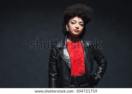 Half Body Shot of a Stylish Young African American Woman in Leather Jacket, Looking at the Camera Against Black Background.