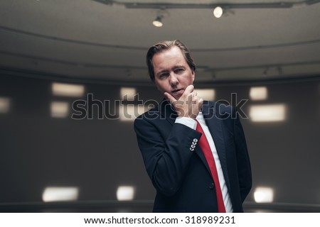 Concerned entrepreneur wearing suit with red tie standing in empty room.