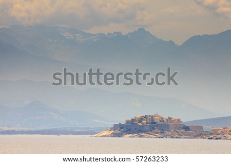 Big mountains with cloudy sky and the city of Calvi, Corsica, France