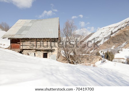 Cottage in winter mountain landscape with blue cloudy sky. Alps. France.