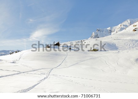 Winter snow mountain landscape with ski traces under blue sky. Sunshine. Rock. Alps. France.