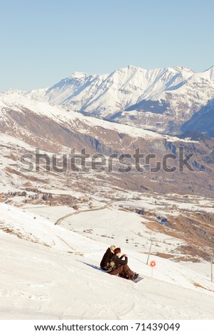Couple snowboarders resting on snow mountain slope. Landscape. Peaks. Blue sky. Relax. Romantic. Young woman. Young man.