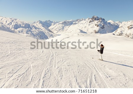Young skiing woman standing in snow mountain landscape with blue sky. Sunshine. Resting. Enjoying the view. Alps. France.
