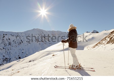 Young skiing woman standing in snow mountain landscape with blue sky. Sunshine. Resting. Enjoying the view. Alps. France.