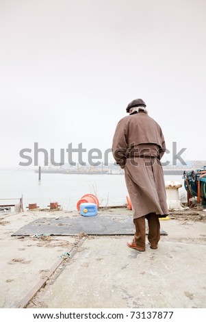 Senior man with raincoat and hat standing in dock. Lonely. Lost.
