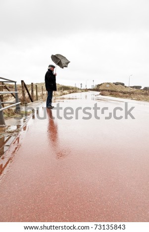 Senior man with broken umbrella by the wind standing on wet road.