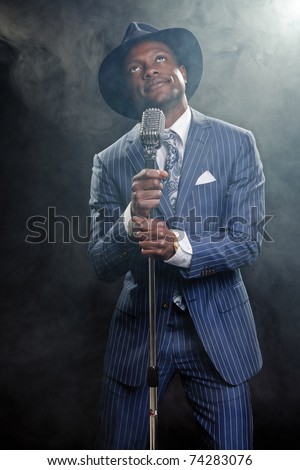 Black man with blue striped suit and blue hat singing. Smoky nightclub