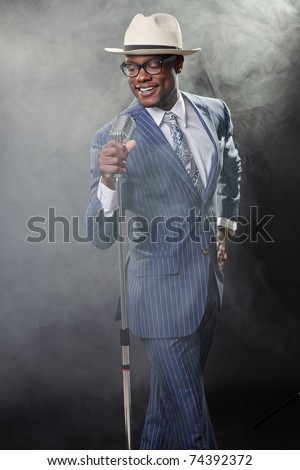 Black man with blue striped suit and blue hat singing in a smoky nightclub like a cotton club