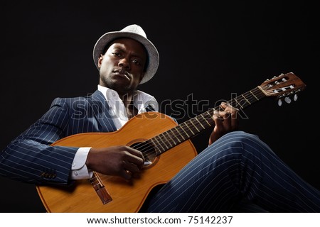 Black jazz musician wearing suit and white hat playing guitar.