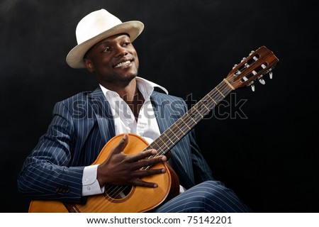 Black jazz musician wearing suit and white hat playing guitar.