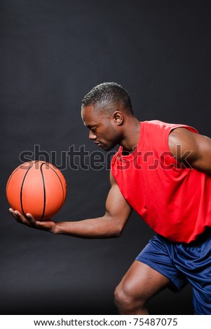 Black basketball player with red shirt and blue shorts holding basketball.