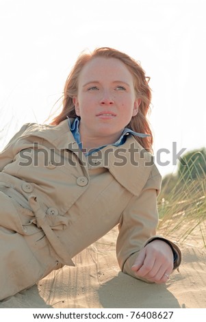 Young woman with red hair lying on sand dune enjoying nature.