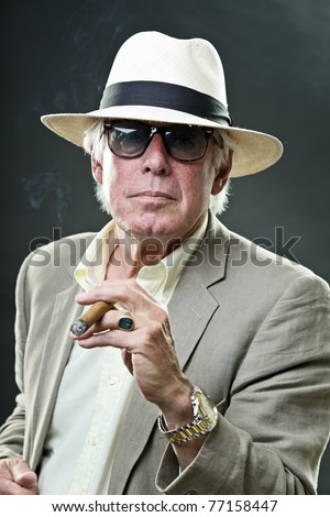 Studio portrait of senior man with hat sunglasses and cigar. Gangster look.