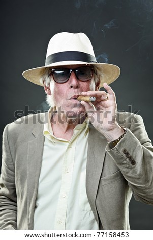 Studio portrait of senior man with hat sunglasses and cigar. Gangster look.