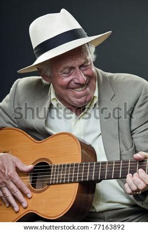 Studio portrait of senior man with hat and guitar. Jazz musician.