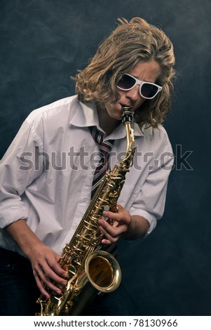 Studio portrait of young hip cool man with saxophone and white sunglasses on black background.