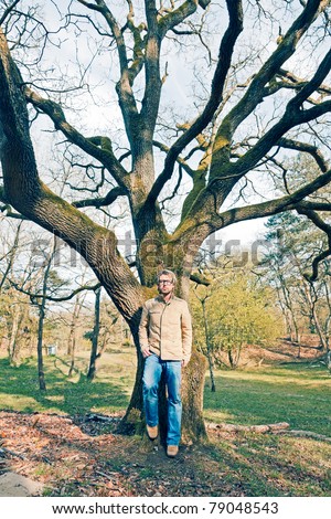 Young casual man enjoying nature standing in front of tree wearing vintage glasses.