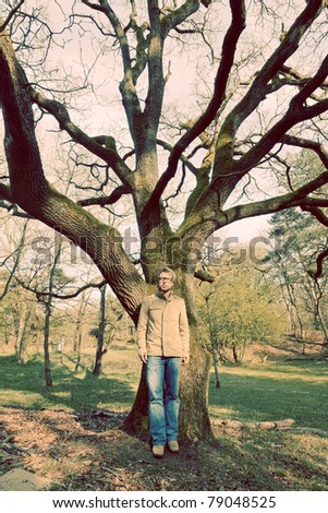Young casual man enjoying nature standing in front of tree wearing vintage glasses.