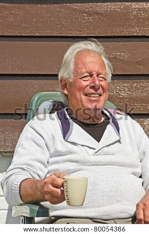 Senior man sitting in garden in chair in summer sun.