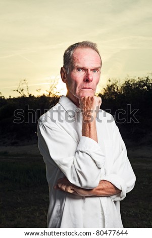 Portrait of senior man with white shirt standing in nature on hot summer day at sunset.