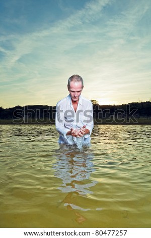 Senior man refreshing in water enjoying nature on hot summer day. Standing in pond.