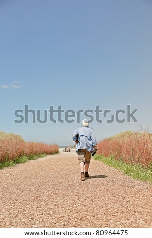 Single senior man walking on path to the beach on hot summer day with clear blue sky.
